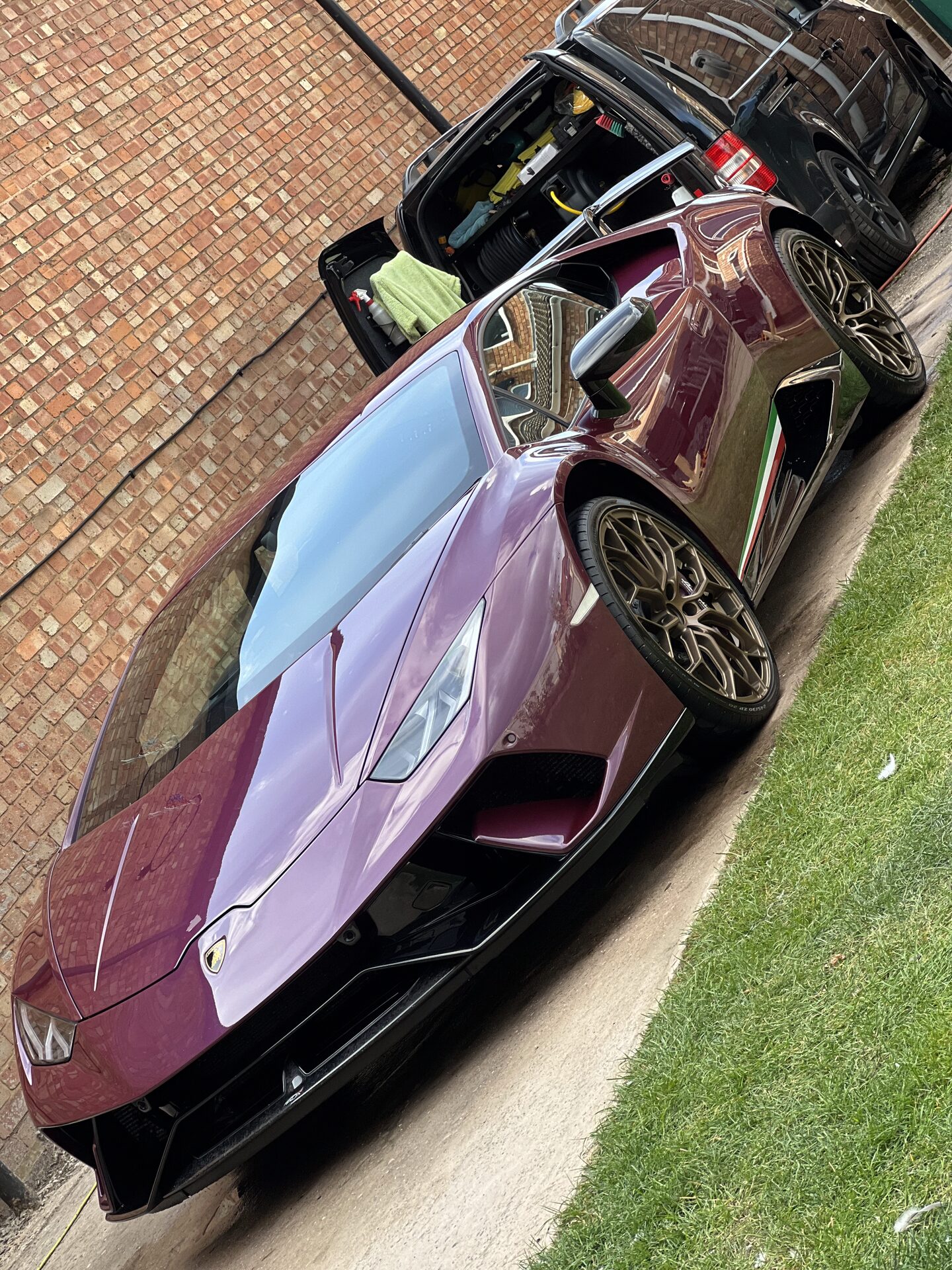 Black sports car covered in thick snow foam pre-wash on a residential driveway